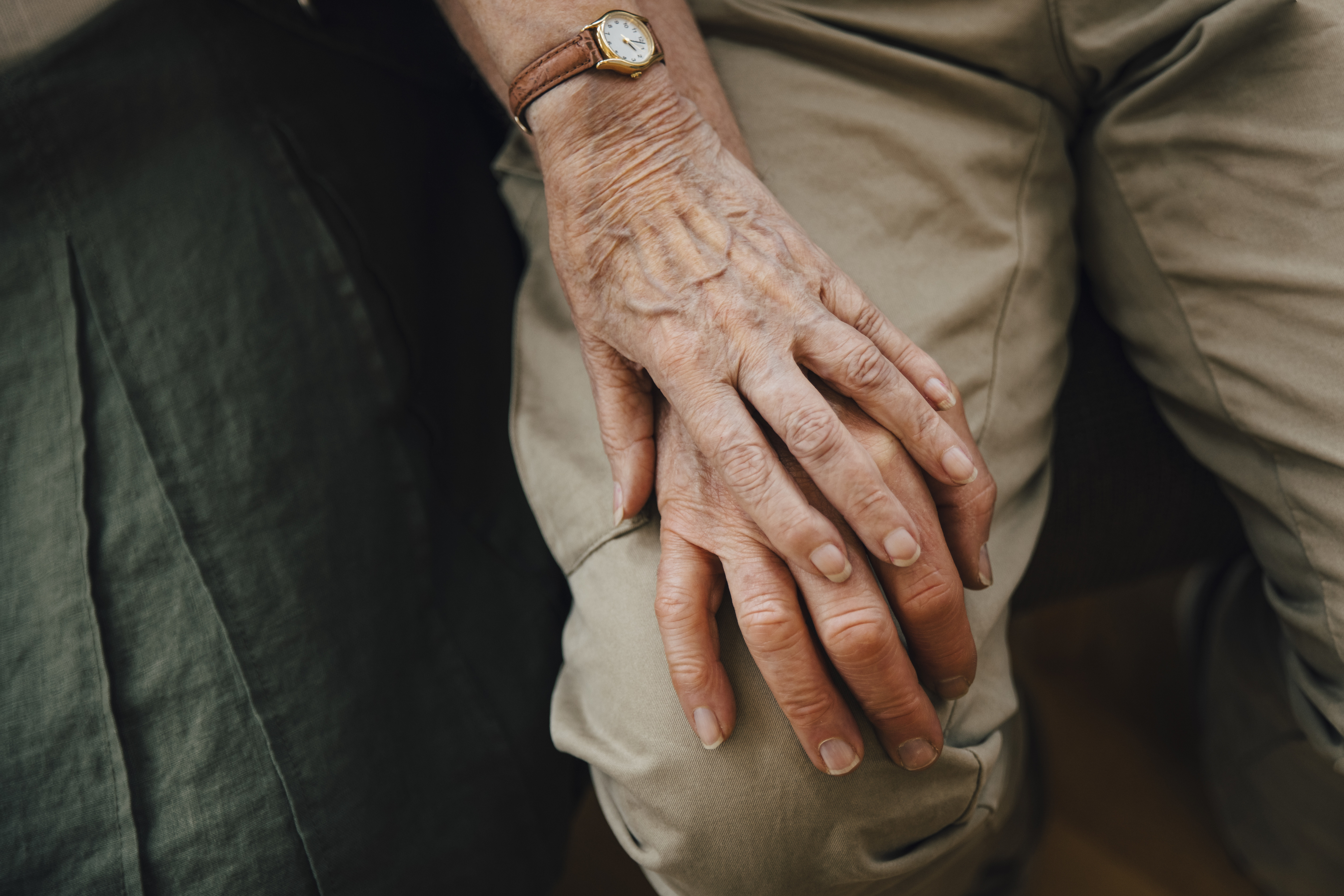 Close-up of an elderly person's hand resting on their lap showcasing a watch