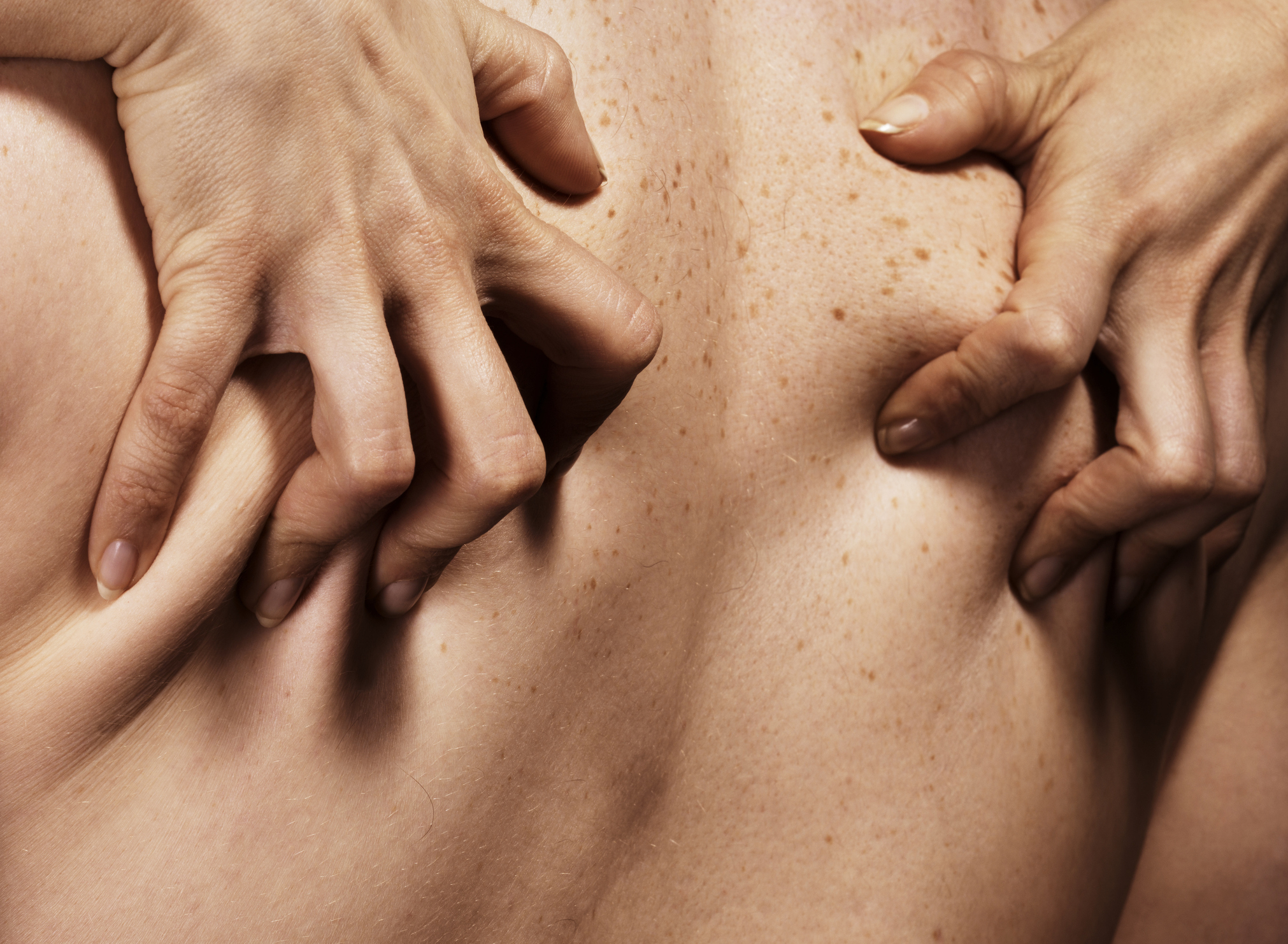 Close-up of a person&#x27;s back with another person&#x27;s hands gently pressing into their skin