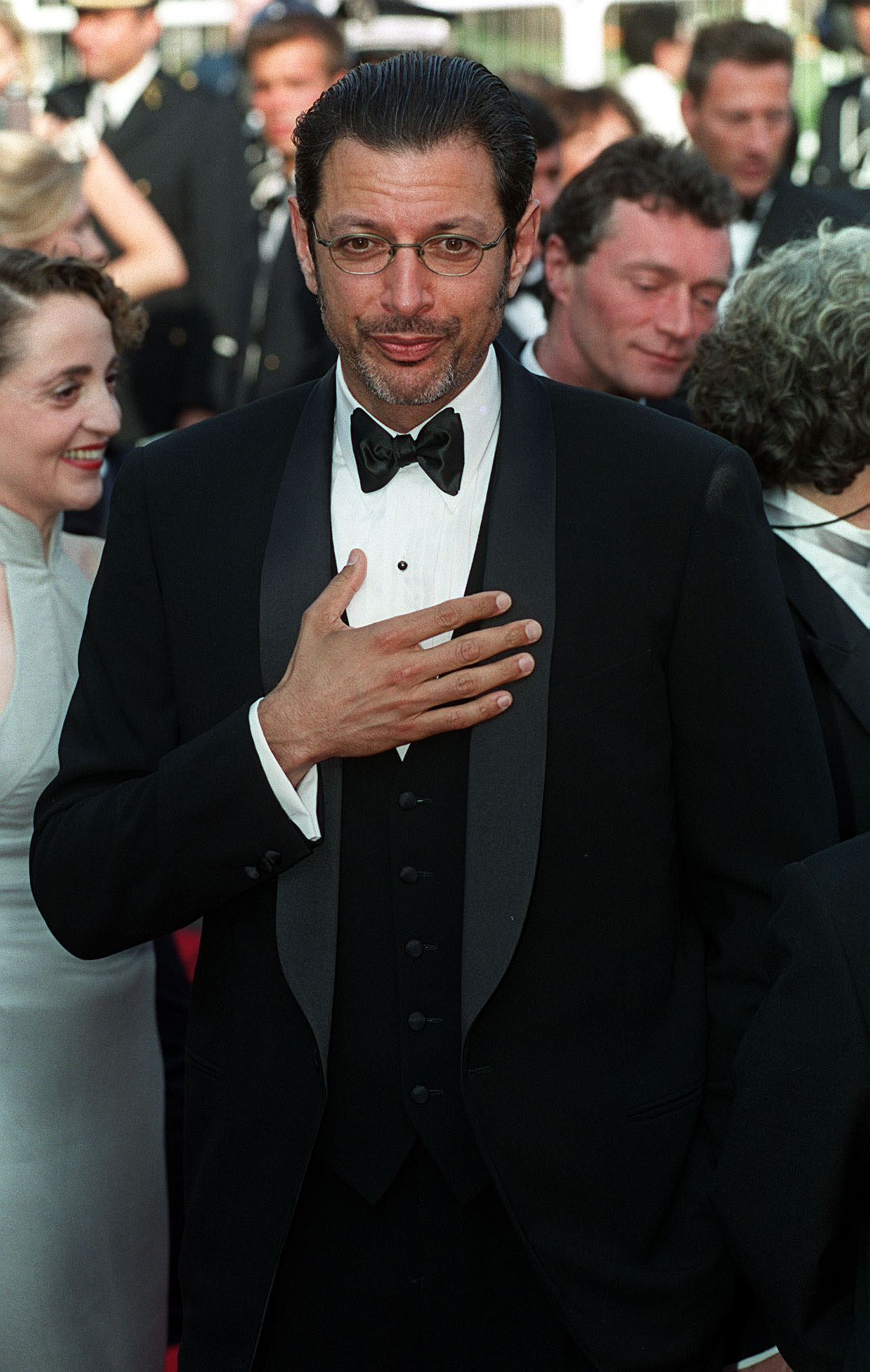 Man at event in black tuxedo with bow tie, hand on chest, smiling