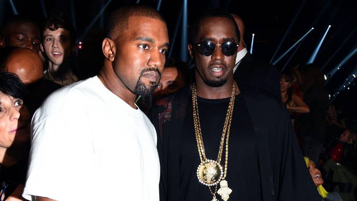 Two men at an event, one in a black shirt and gold chain, the other in a black jacket