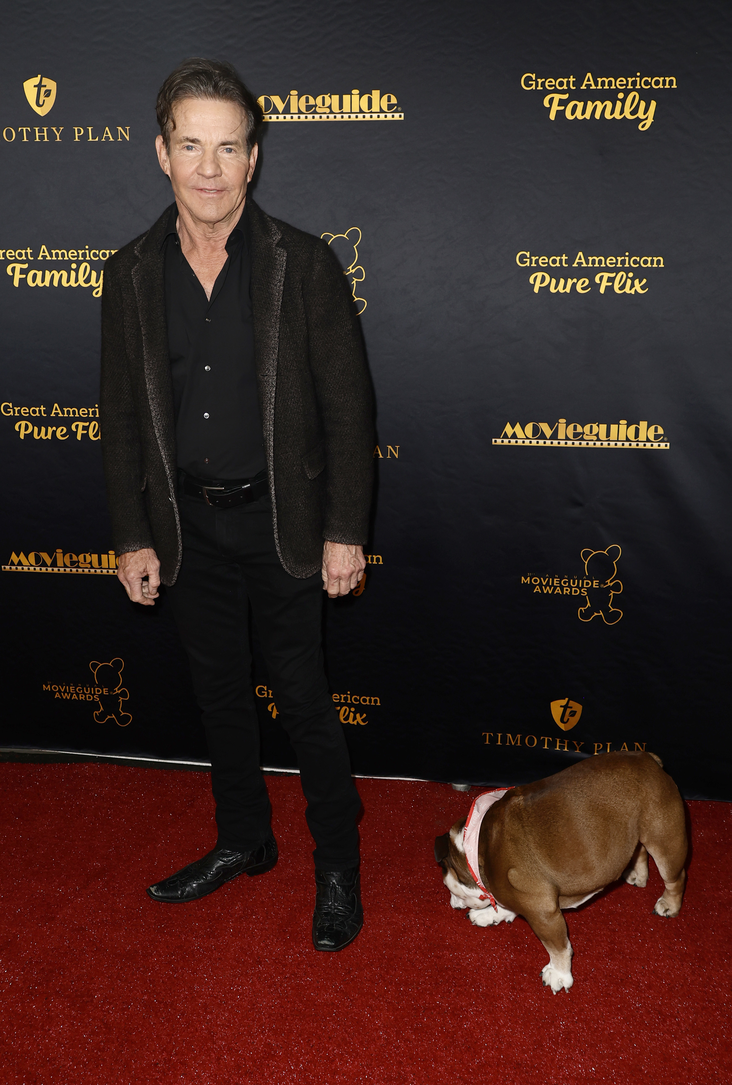 Man in a black shirt and blazer with jeans and a bulldog on a leash on the red carpet