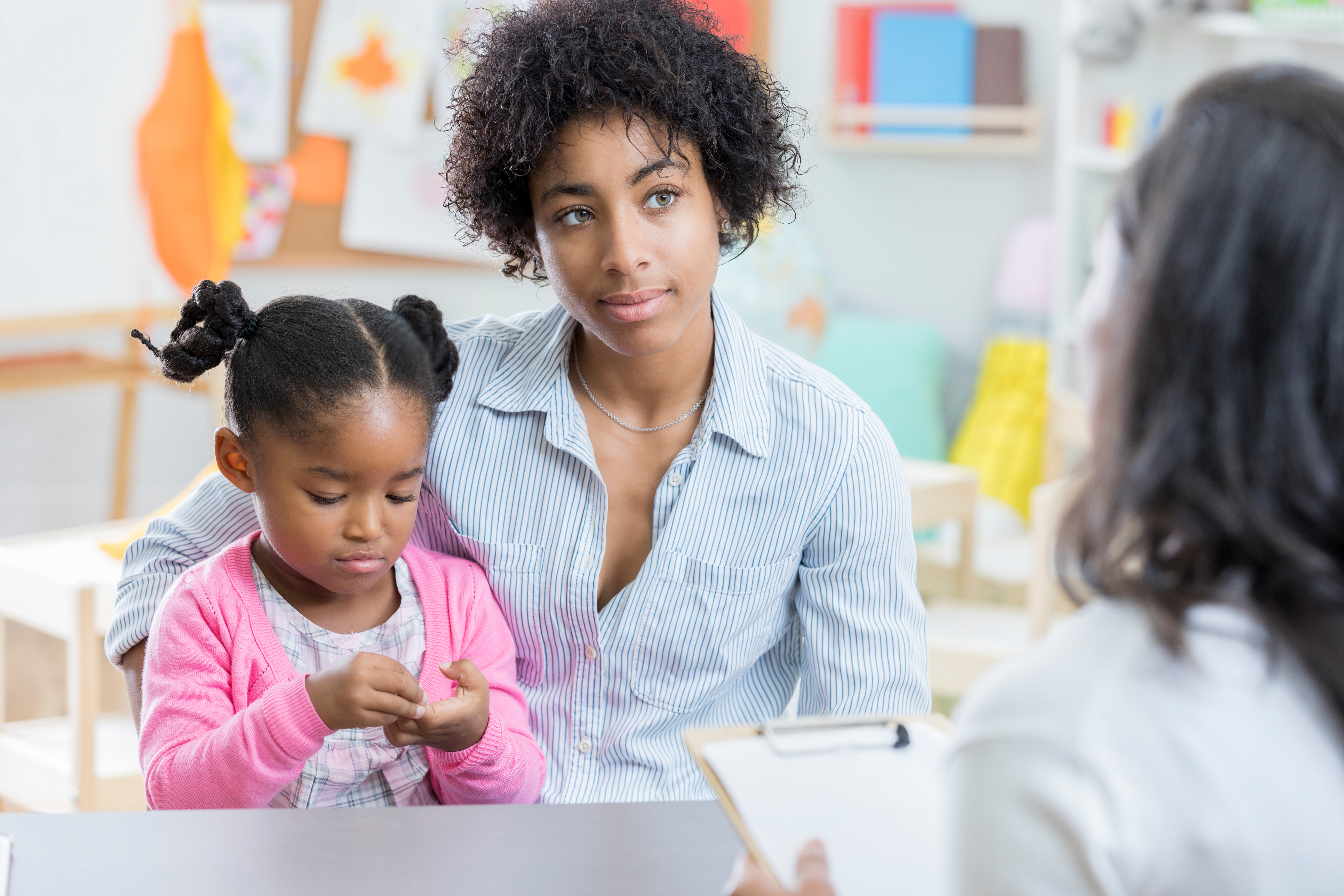 Parent and child sitting together, interacting with a third individual across a table, in what appears to be a school setting