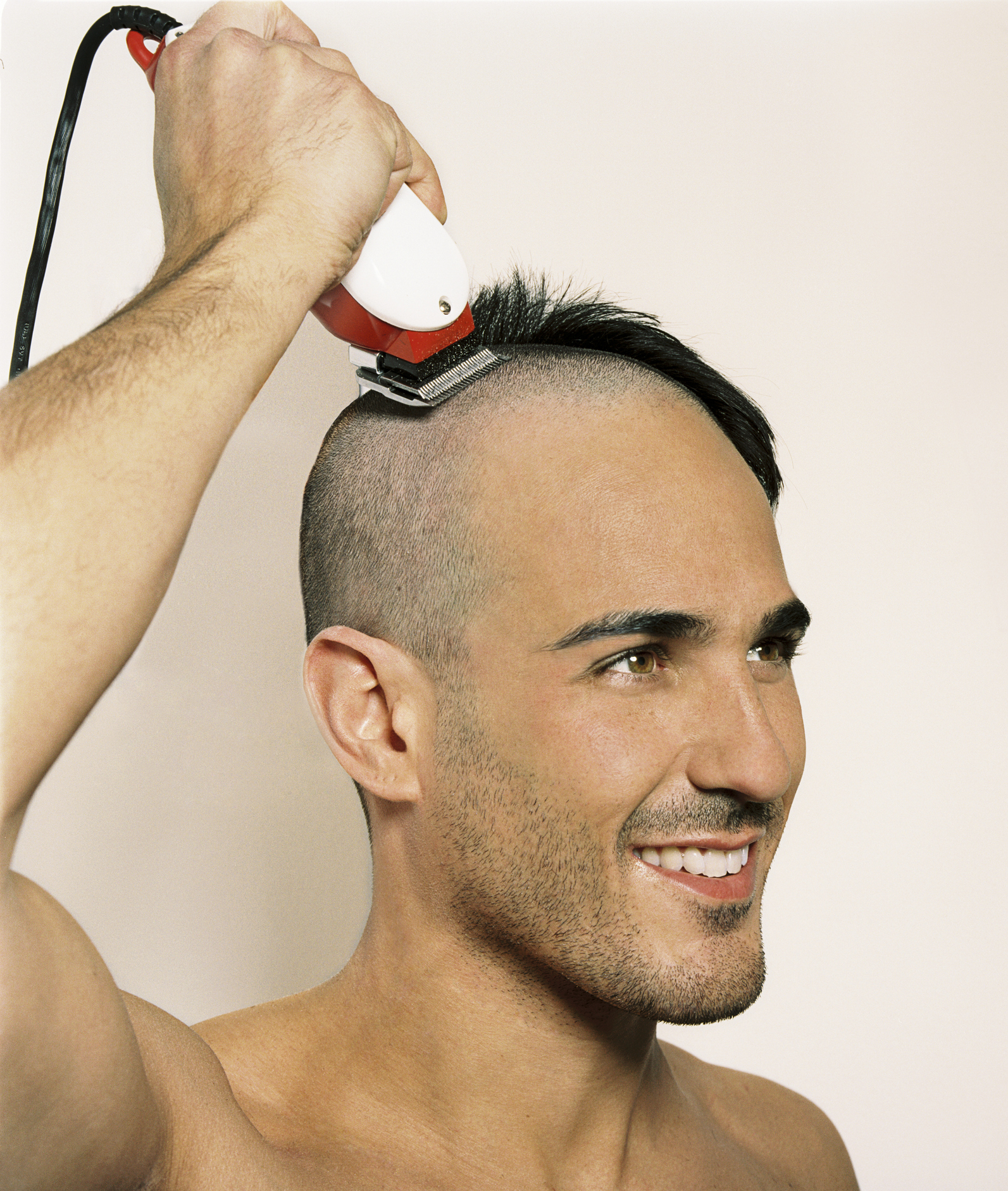 Person shaving head with electric clippers, visible hair growth on sides, smiling
