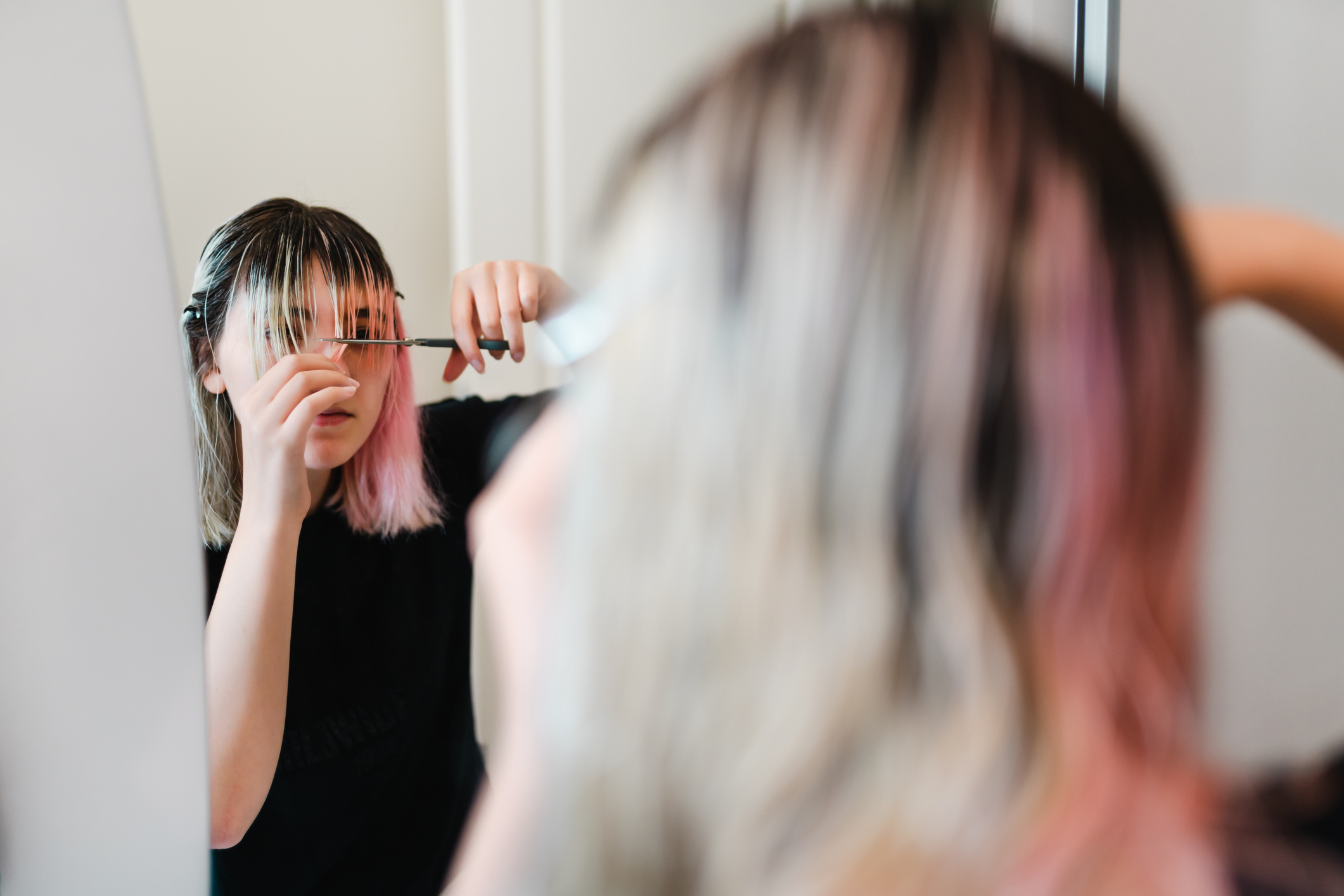 Person trimming their bangs in front of a mirror