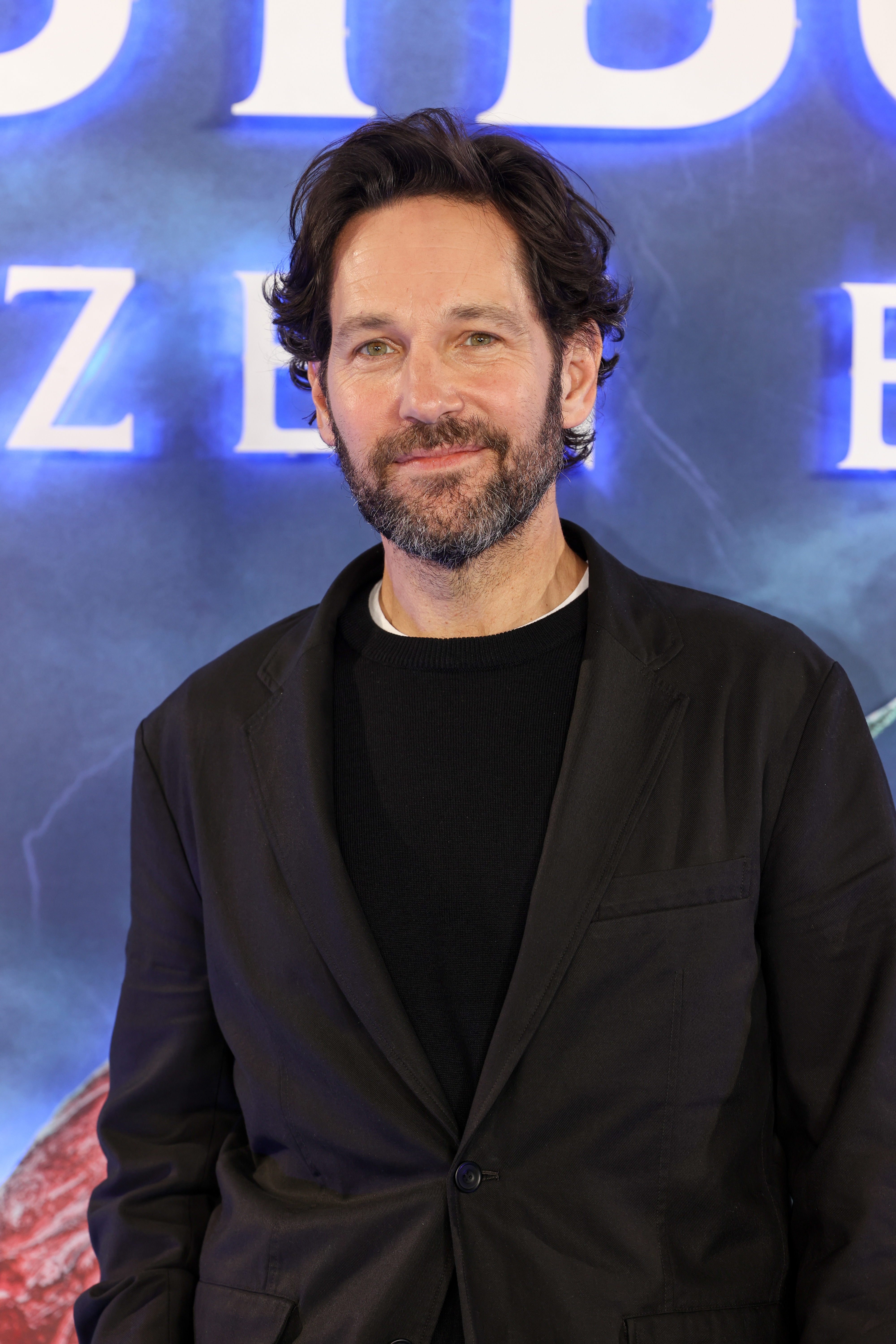 Paul Rudd in a black suit stands smiling at a &quot;Ant-Man and the Wasp: Quantumania&quot; event