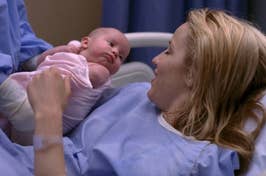 Quinn from Glee smiling and holding her baby in a hospital bed