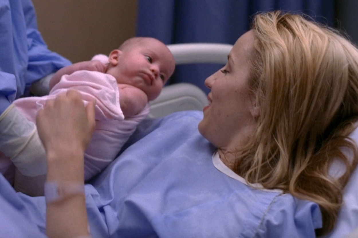 Quinn from Glee smiling and holding her baby in a hospital bed