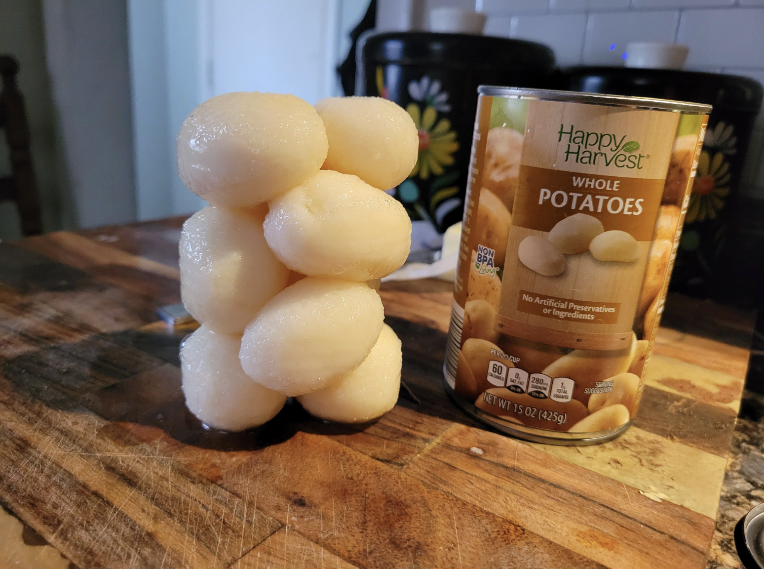 A stacked whole canned potatoes next to its container on a kitchen counter
