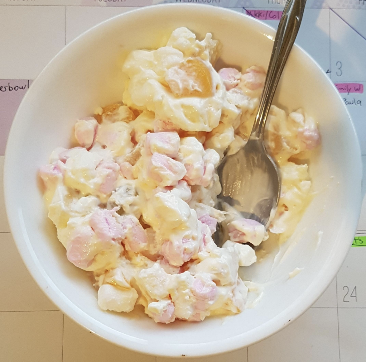 Bowl of fruit salad with creamy dressing and a spoon on a paper calendar background