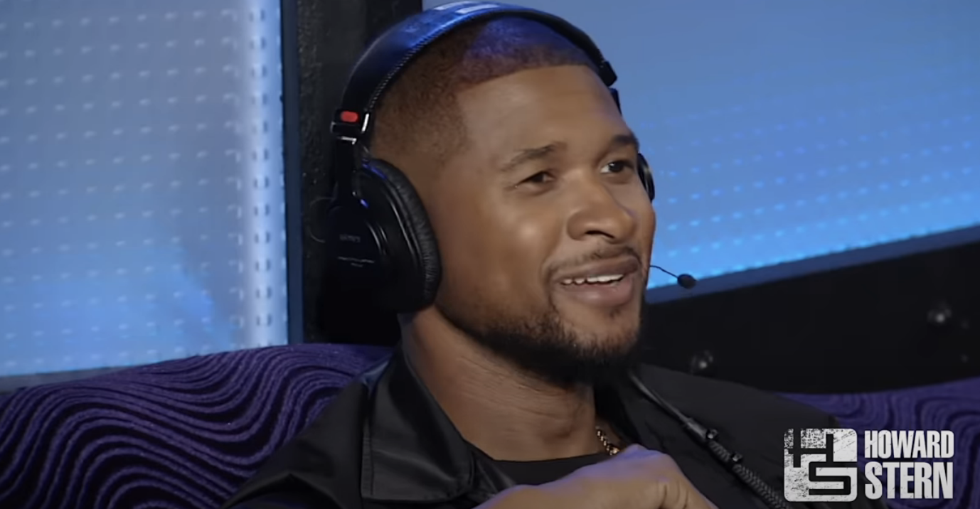 Usher wearing headphones smiles during an interview, mic visible