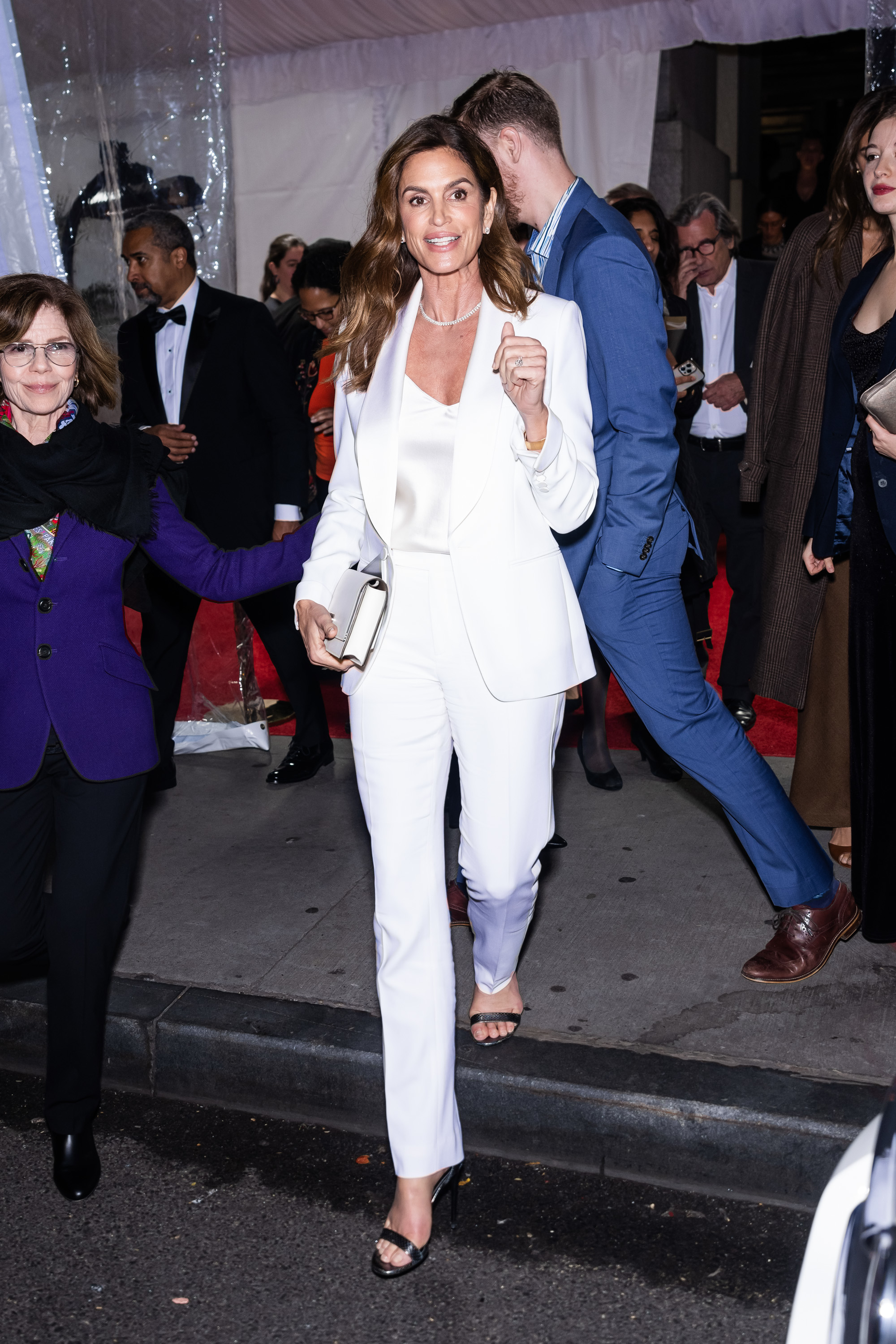 Woman in white suit with lapels and holding a clutch, walking at an event