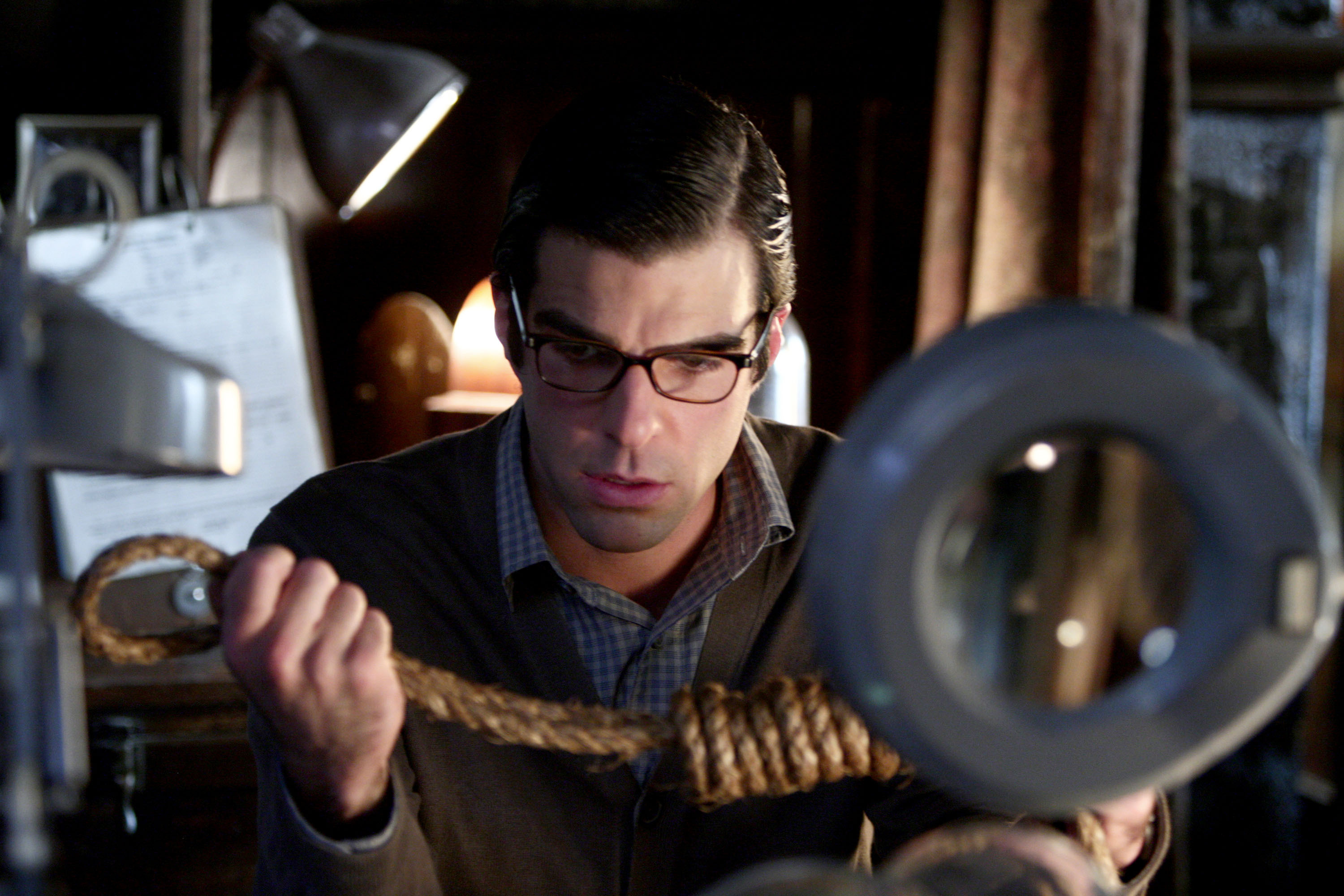 Zachary wearing glasses and examines a rope in a dimly lit room with vintage equipment