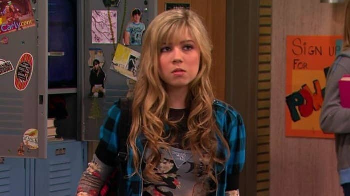Character Sam from the show &quot;iCarly&quot; stands in front of lockers, wearing a layered shirt and expressing surprise