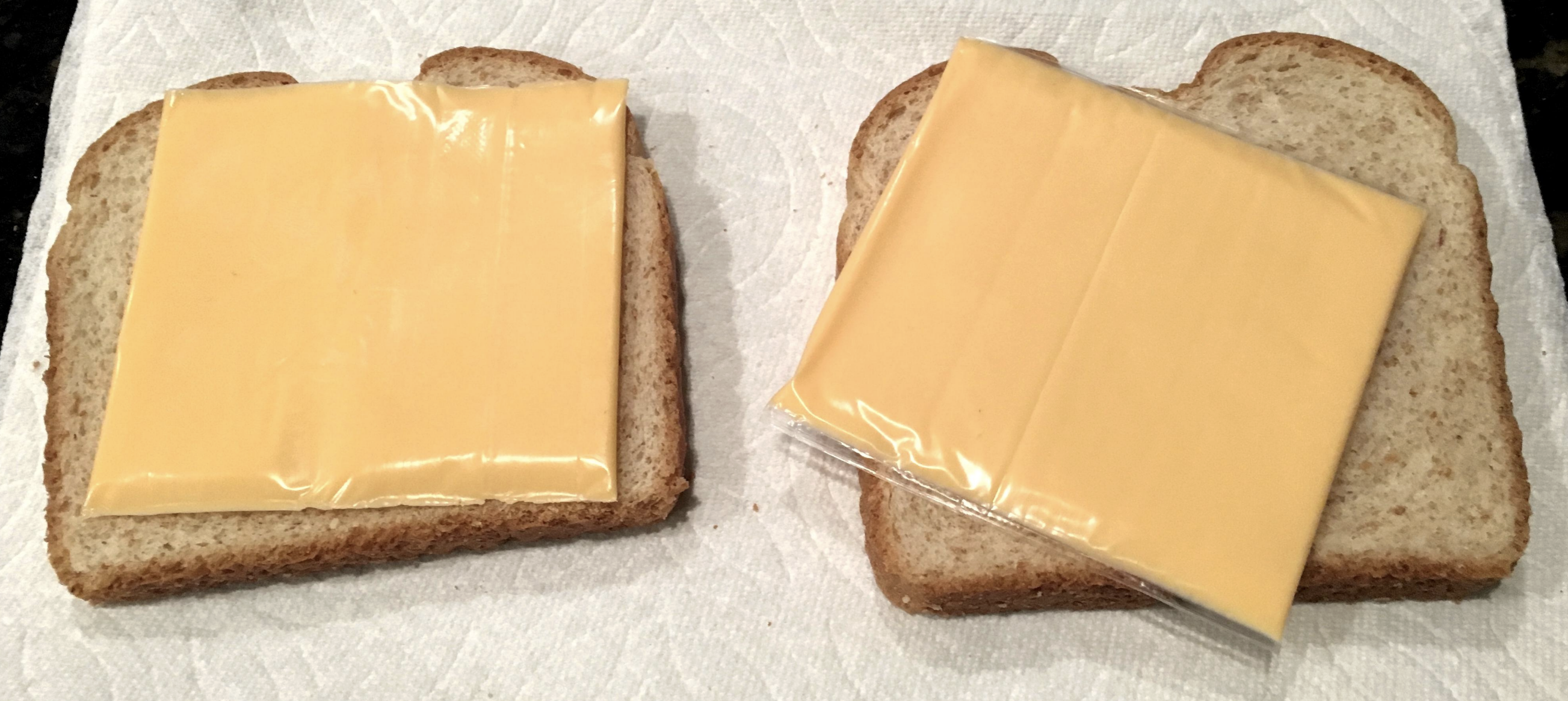 Two slices of bread with a single cheese slice on each, one with wrapper partially on