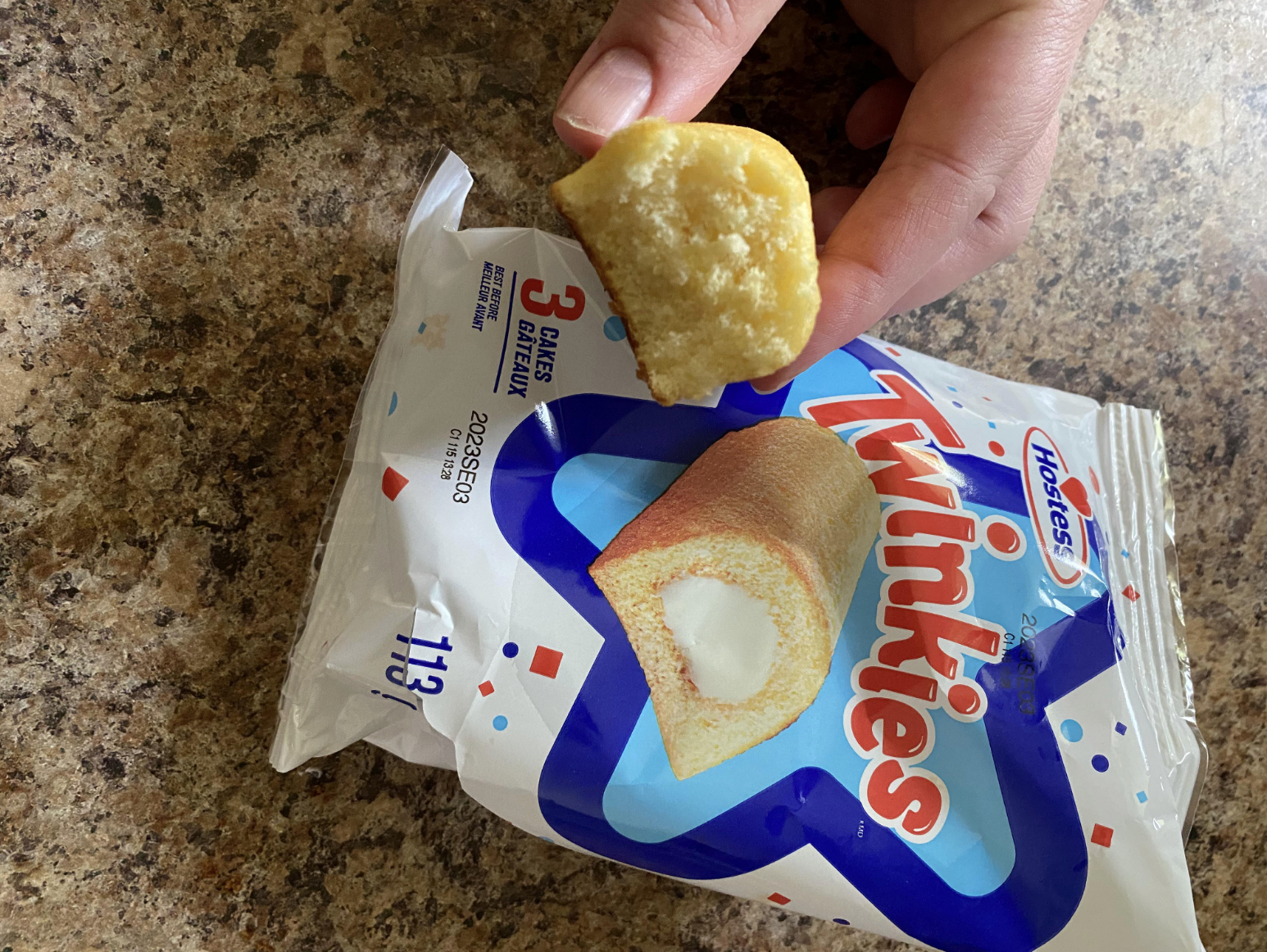Person holding a bitten Twinkie over an open Twinkies snack package