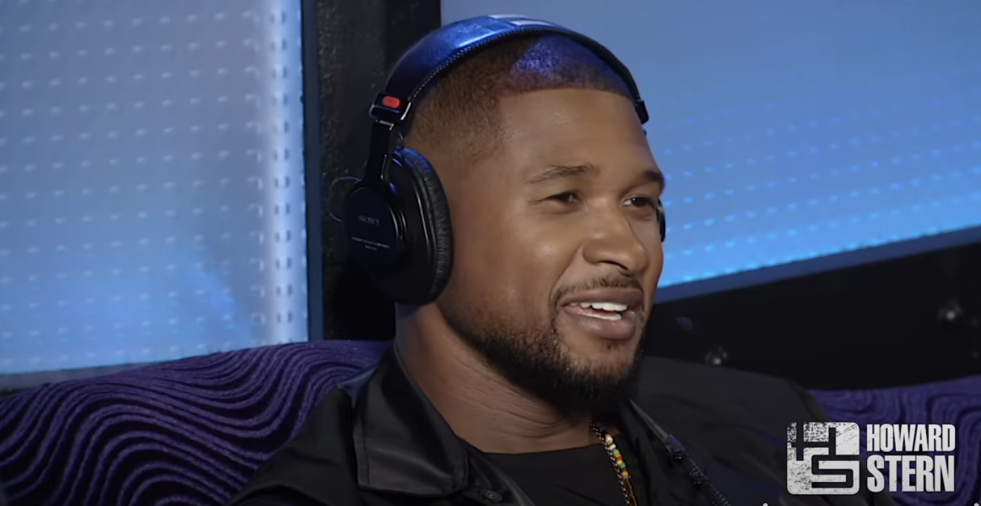 Usher with headphones smiling in a studio, text &quot;Howard Stern&quot; visible in the background