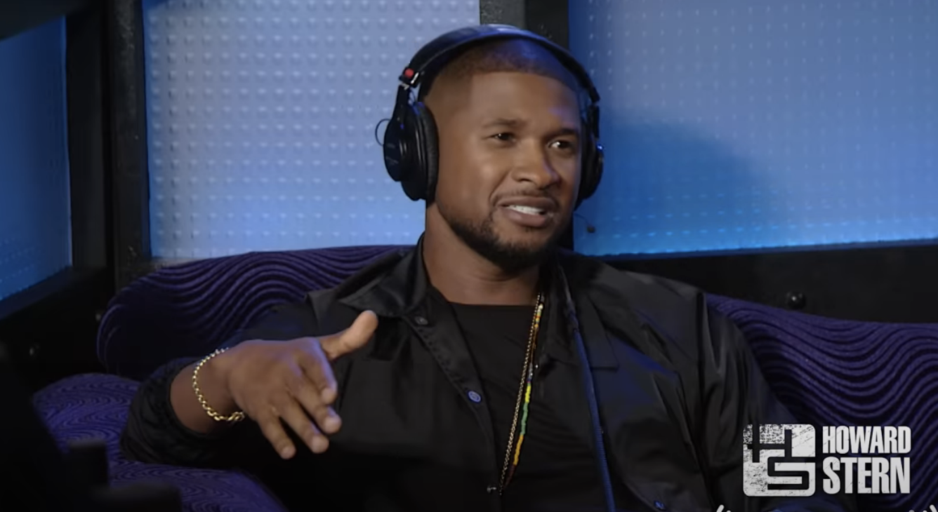 Usher in a studio wearing headphones, speaking into a microphone