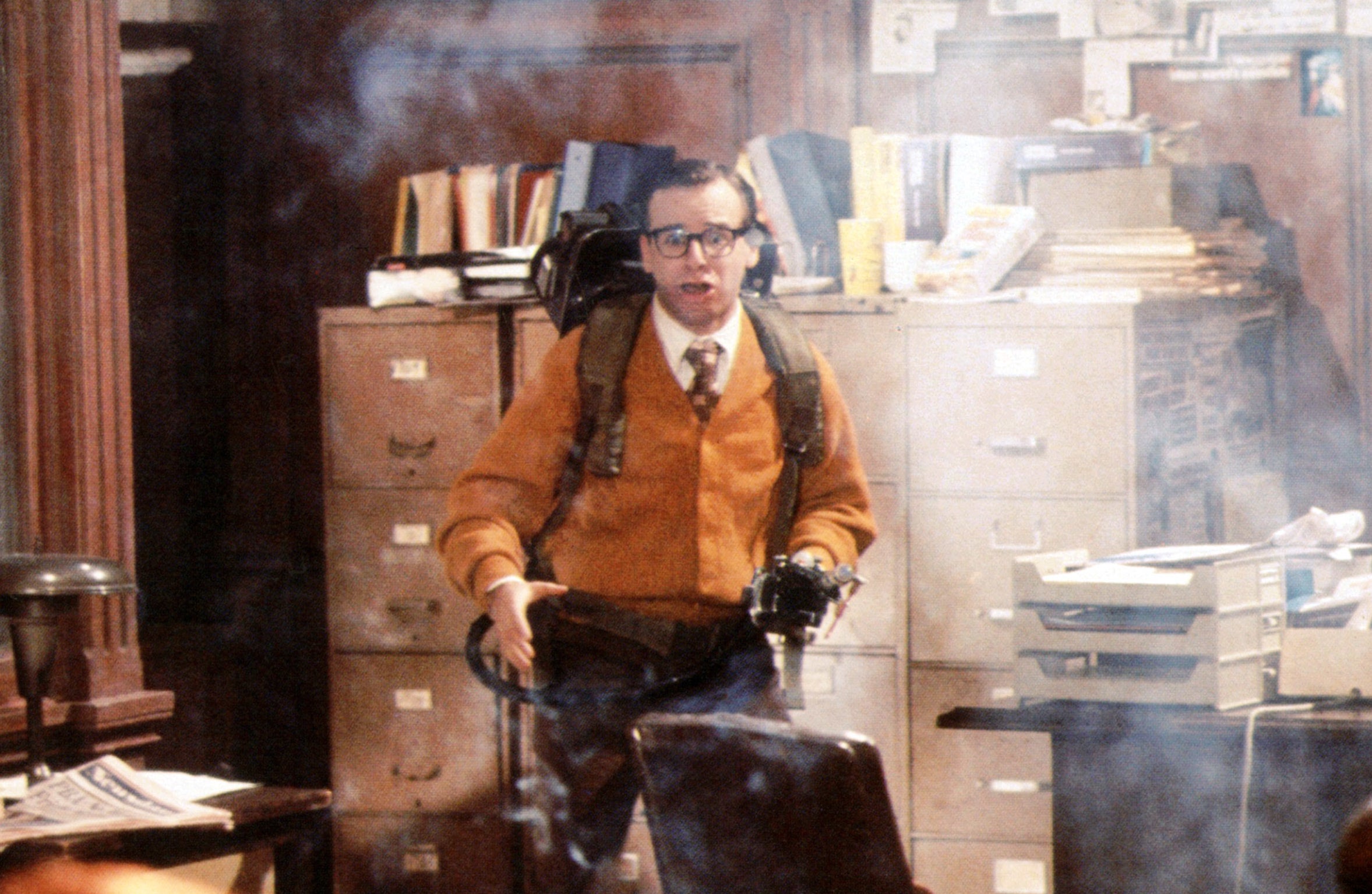 Office in disarray with Rick as a Ghostbusters holding a smoking ghost trap