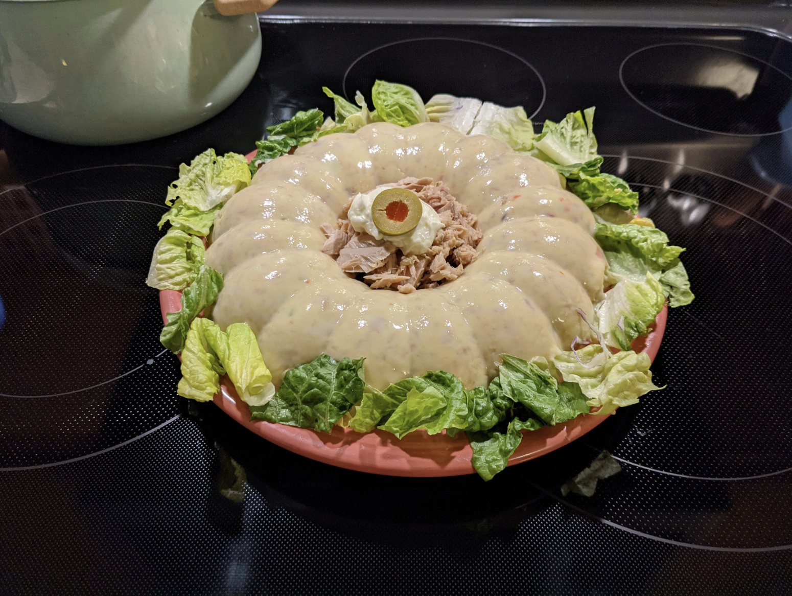 A gelatin mold filled with tuna and garnished with lettuce and olives, presented on a kitchen counter