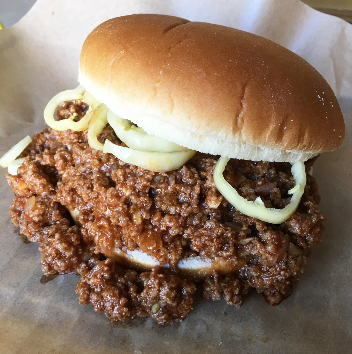 A close-up of a sloppy joe sandwich with ground beef and onions on a bun