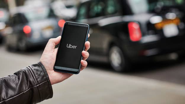 Hand holding smartphone with Uber app on screen, taxis in background