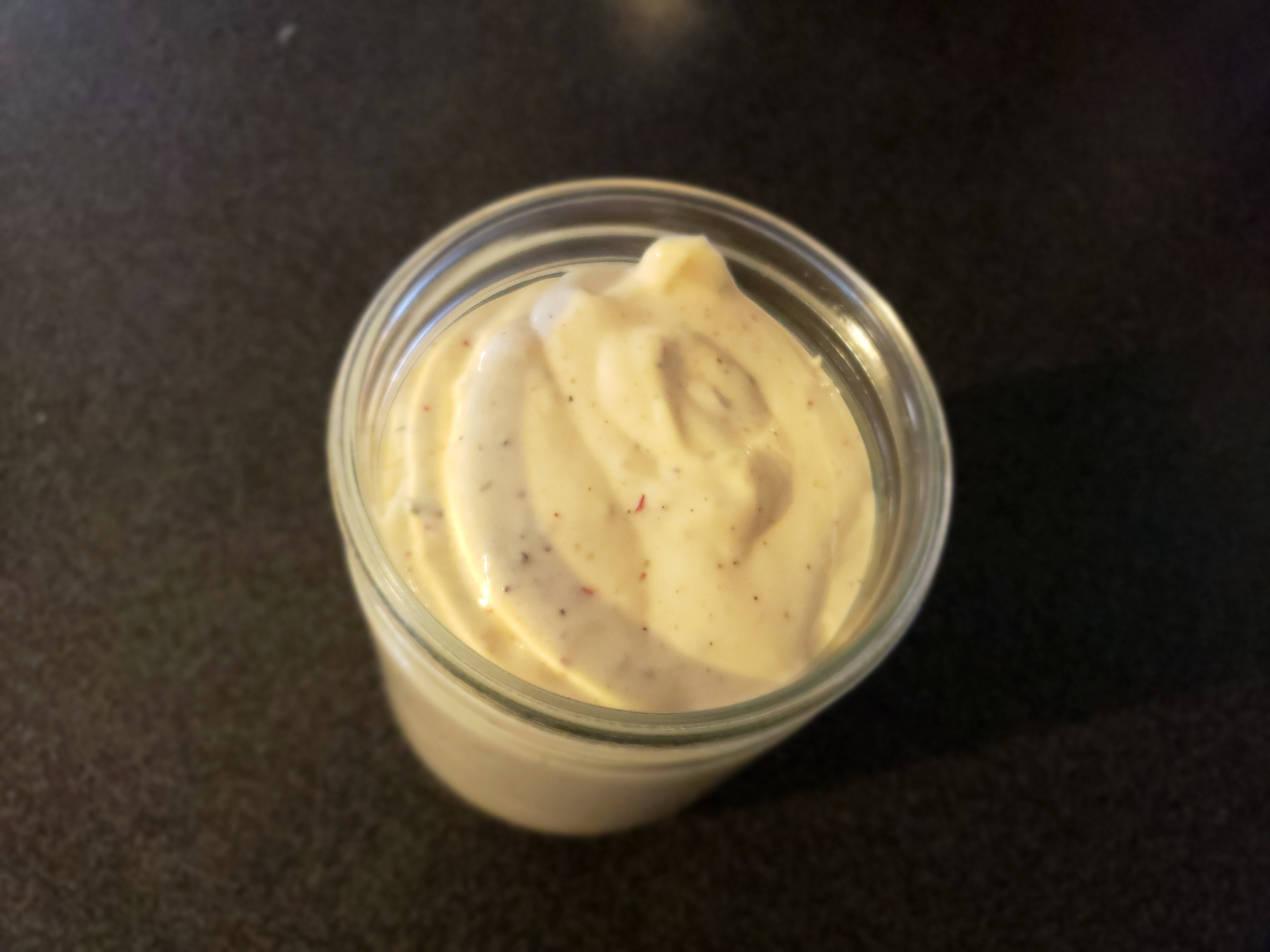 A jar of creamy Ranch with specks of herbs on a dark countertop