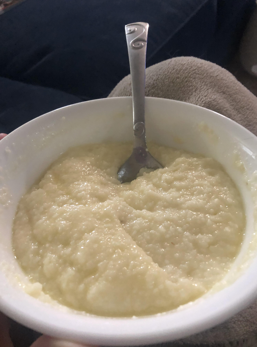 Bowl of creamy grits with a spoon, close-up, held by a person