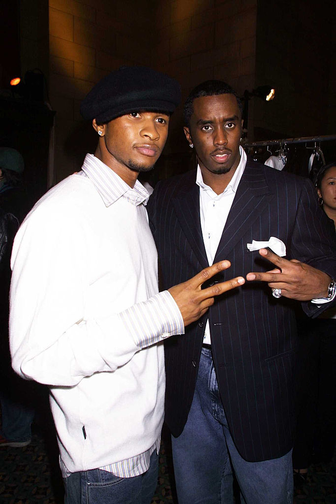 Usher and Diddy in stylish attire, one in a sweater and flat cap, the other in a pin-striped suit, posing for a photo