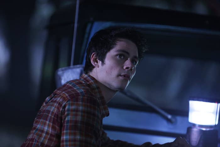 Dylan O&#x27;Brien as Stiles Stilinski in a plaid shirt, looking concerned, with a flashlight in a dimly lit scene from Teen Wolf