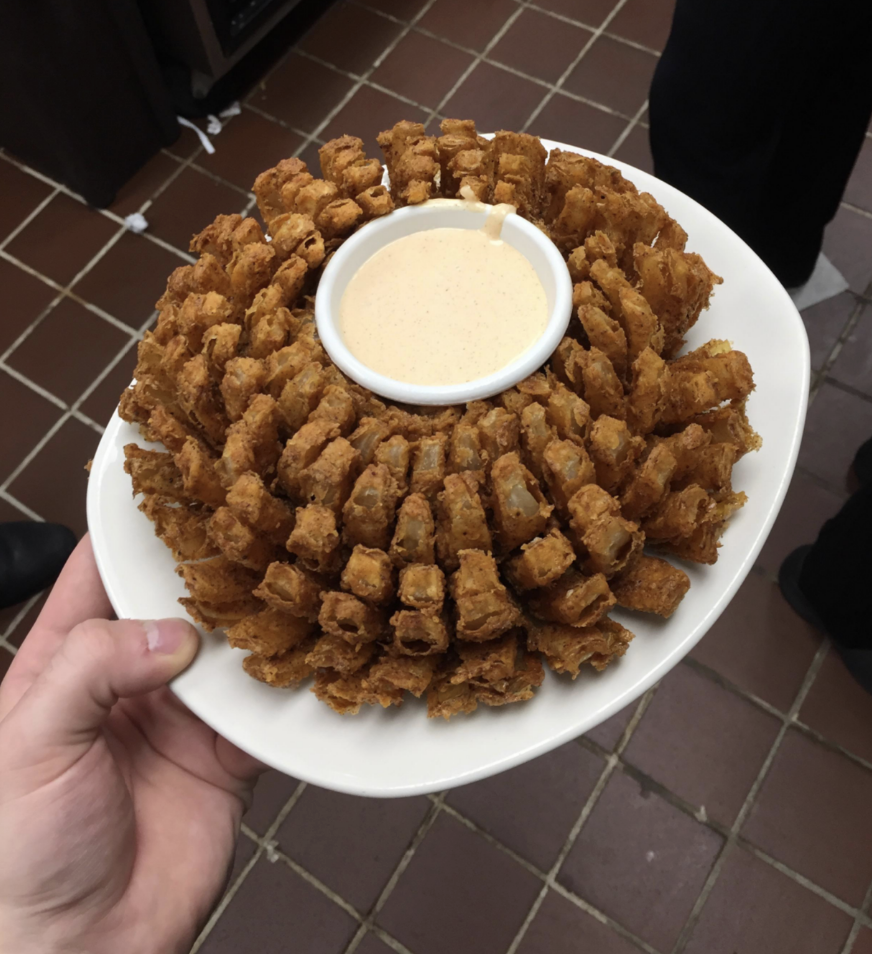 Person holding a plate with a blooming onion and dipping sauce