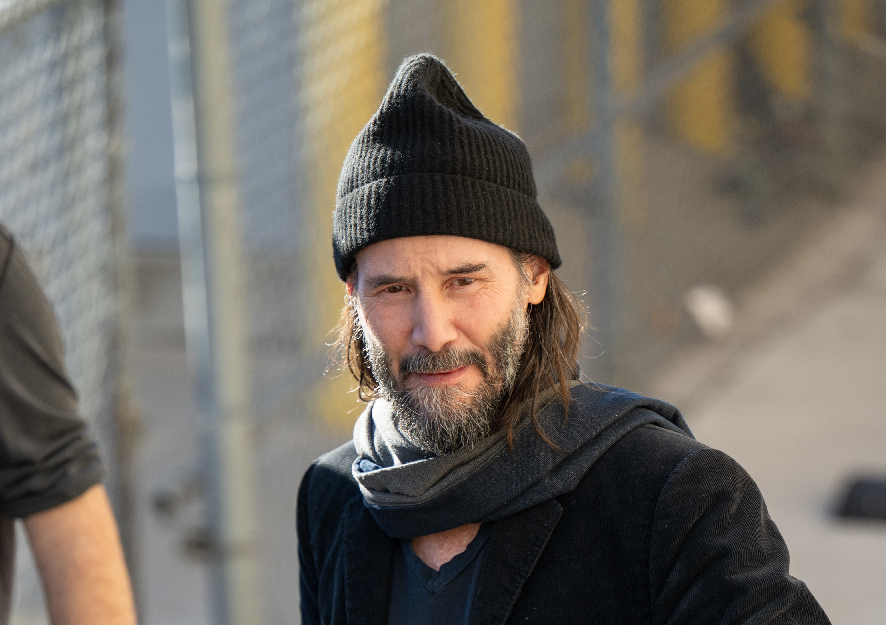 Man in beanie and scarf smiles outdoors. Celebrity, casual style