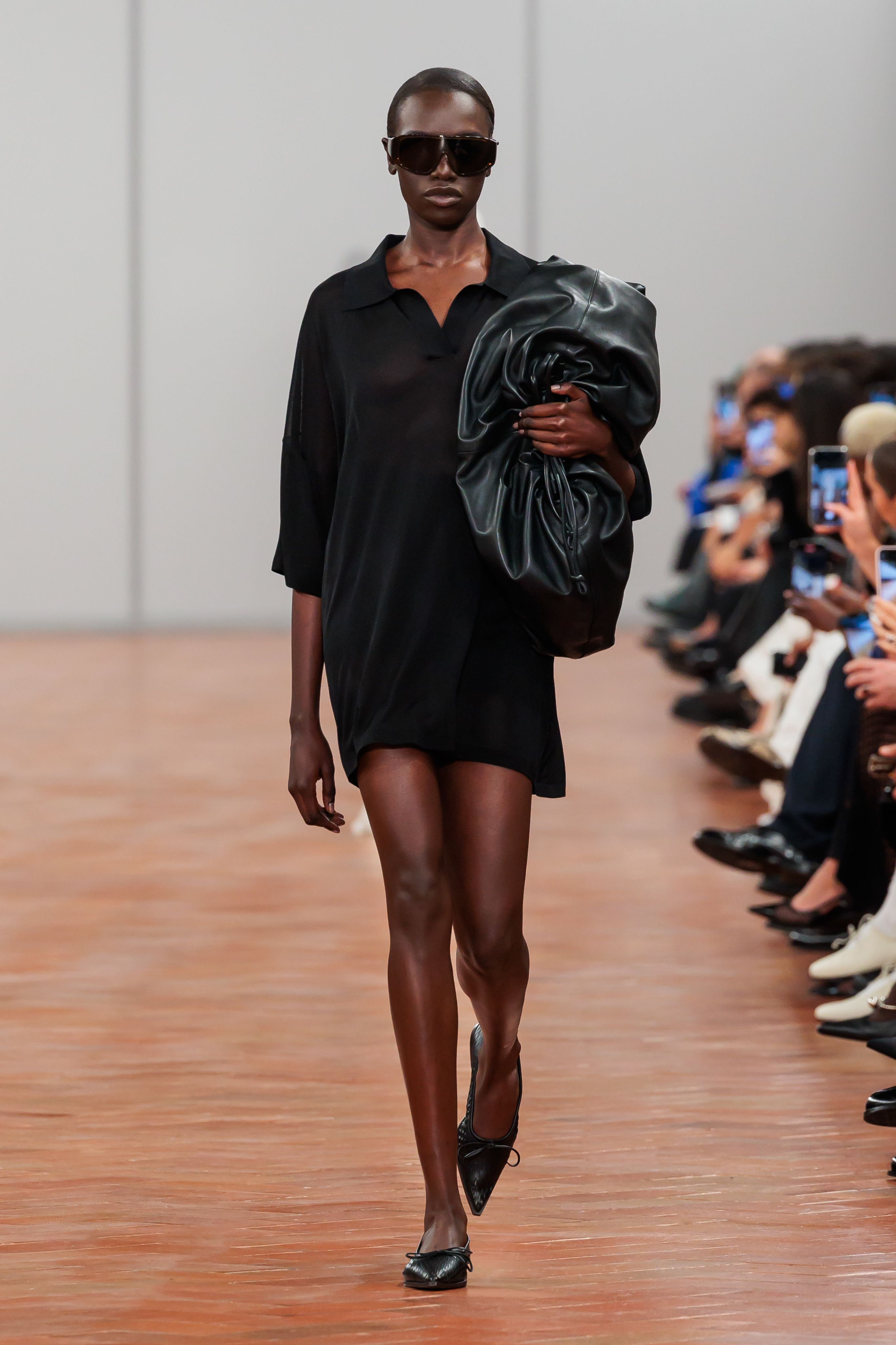 Model on runway showcasing a black dress and large ruffled green sleeve accessory