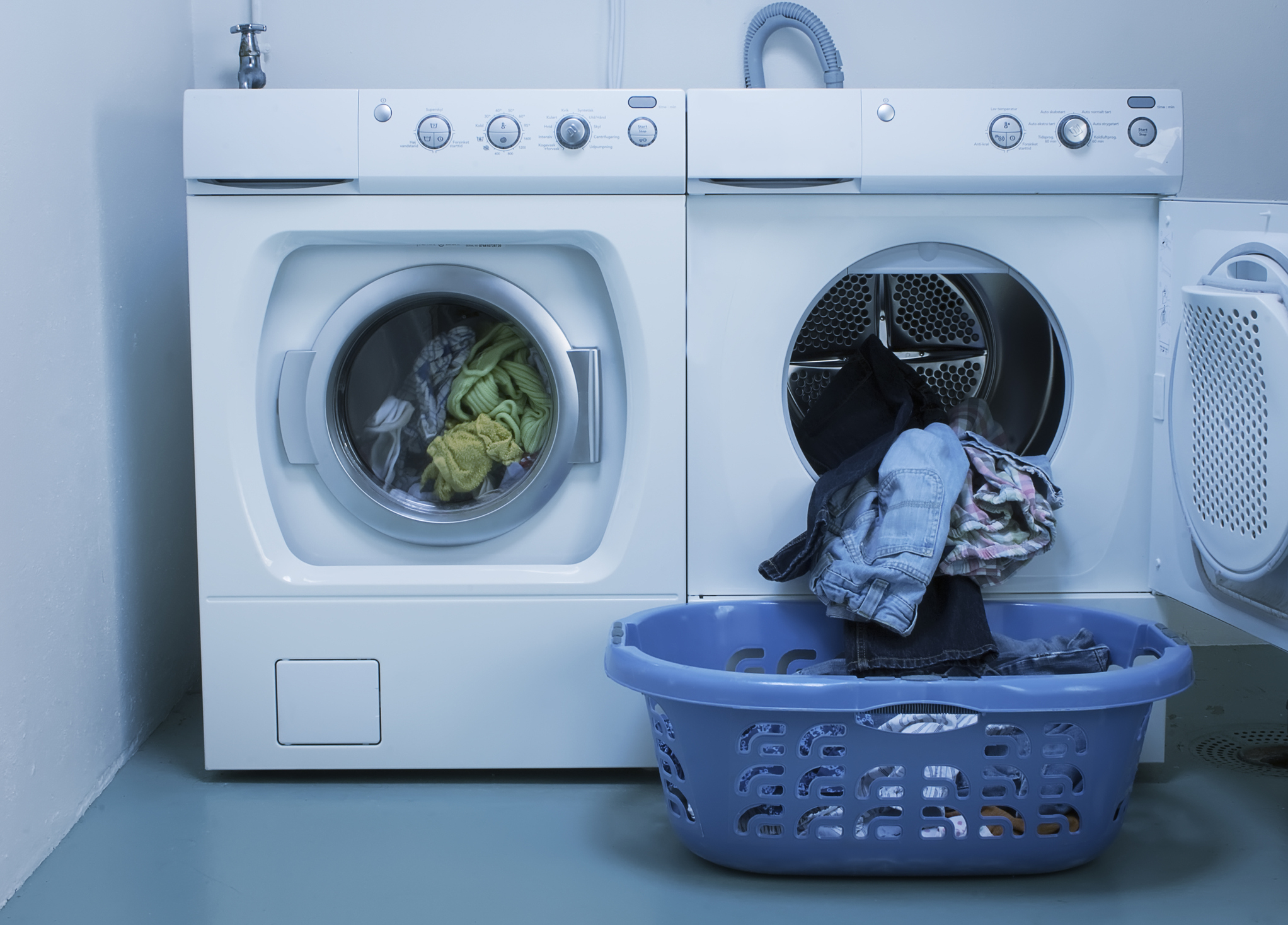 Washing machine in mid-cycle next to a dryer with an open door, and a laundry basket with clothes in front