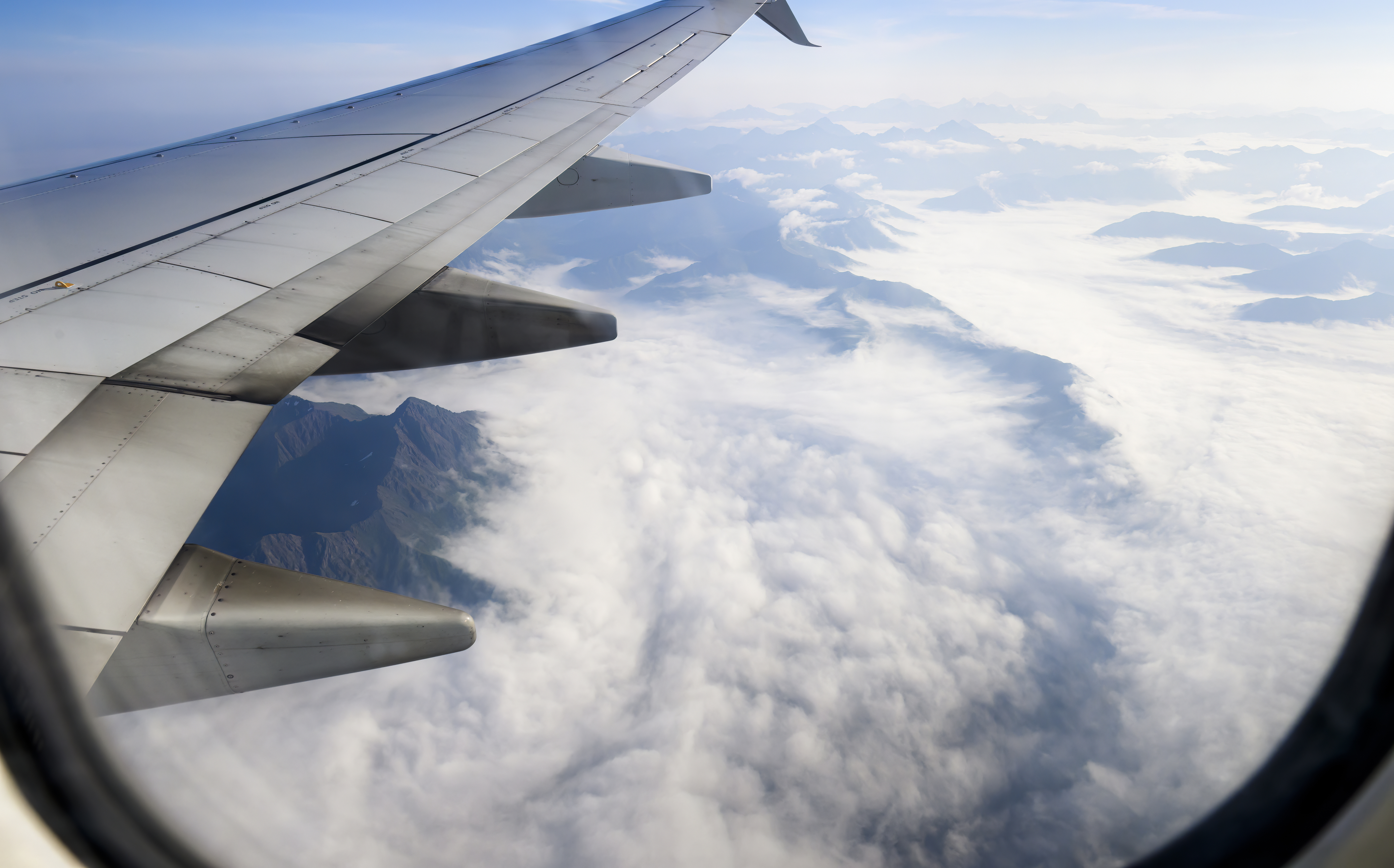 Airplane wing over clouds with mountains in the distance, viewed from window