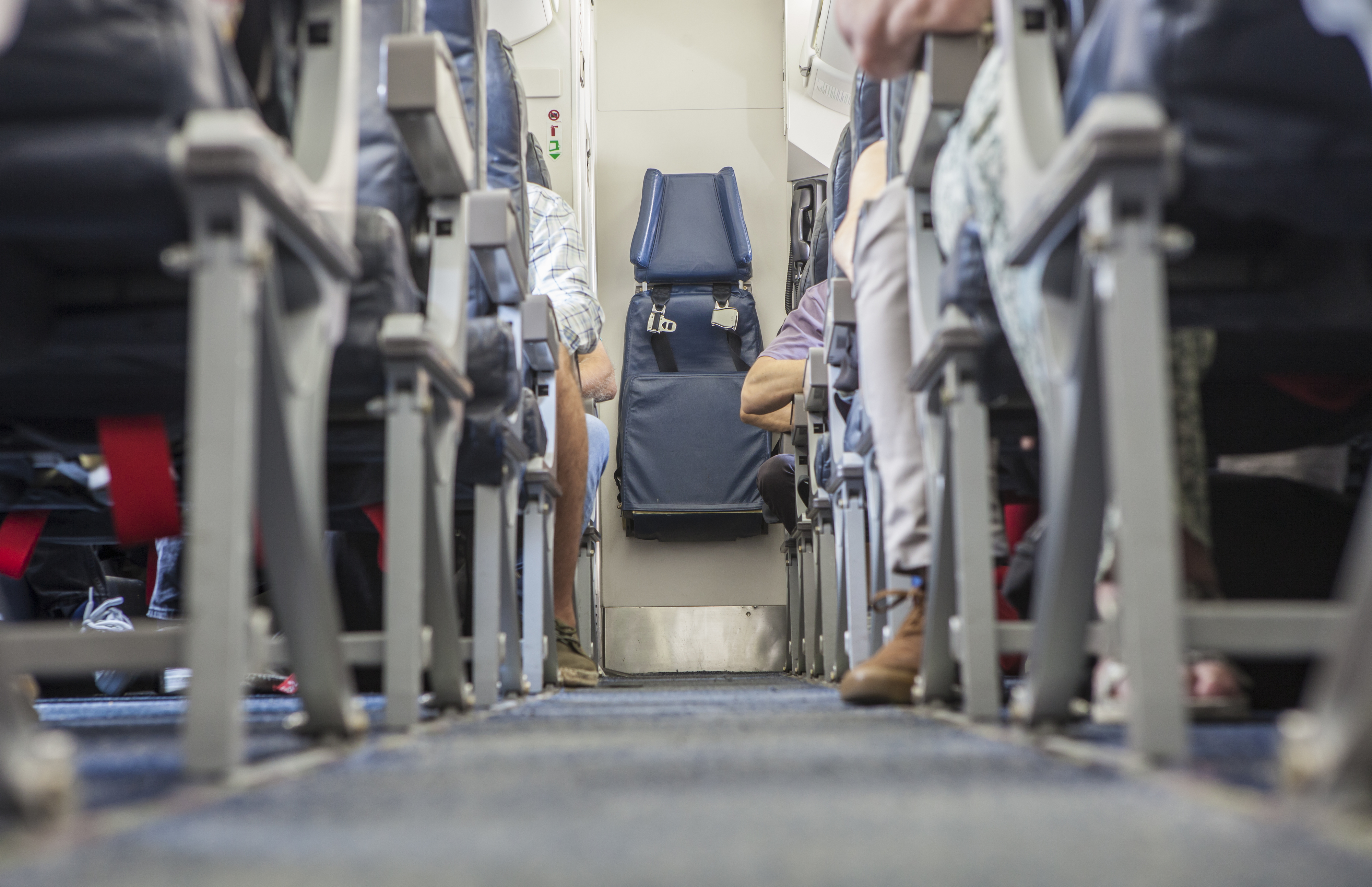 View down an airplane aisle with passengers seated on either side, facing forward