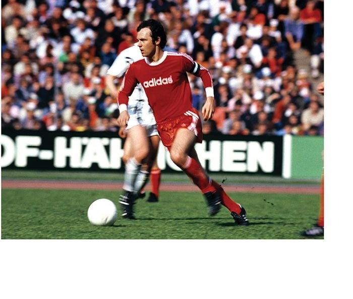 A soccer player in a red and white Adidas uniform dribbles the ball on the field