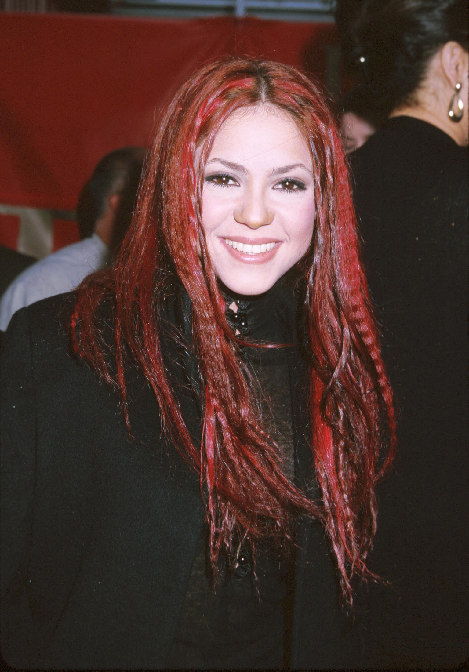 Smiling woman with long red-streaked hair, wearing a black outfit on the red carpet