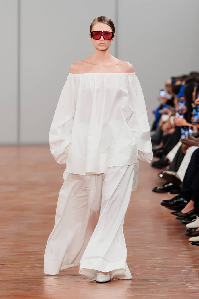 Model in an off-shoulder billowy top and wide-leg trousers walks the runway