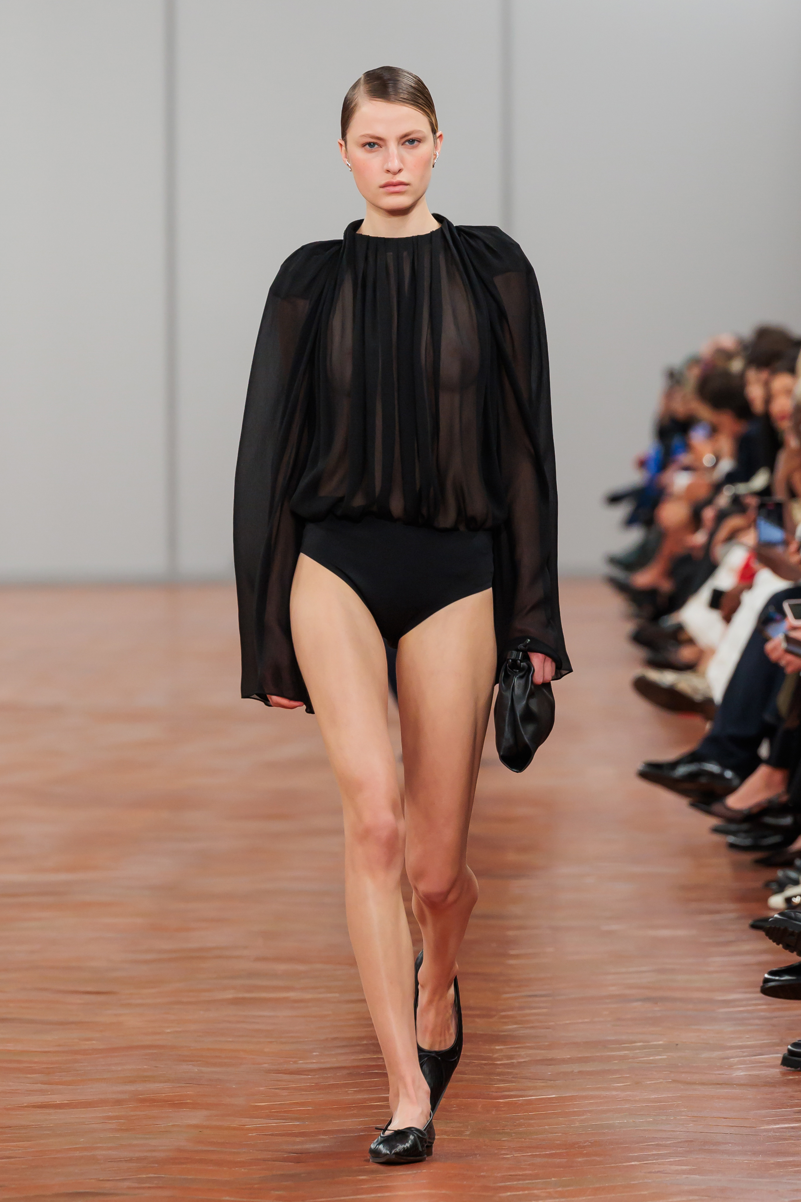 Model on runway wearing a sheer black blouse with billowing sleeves and black bottoms