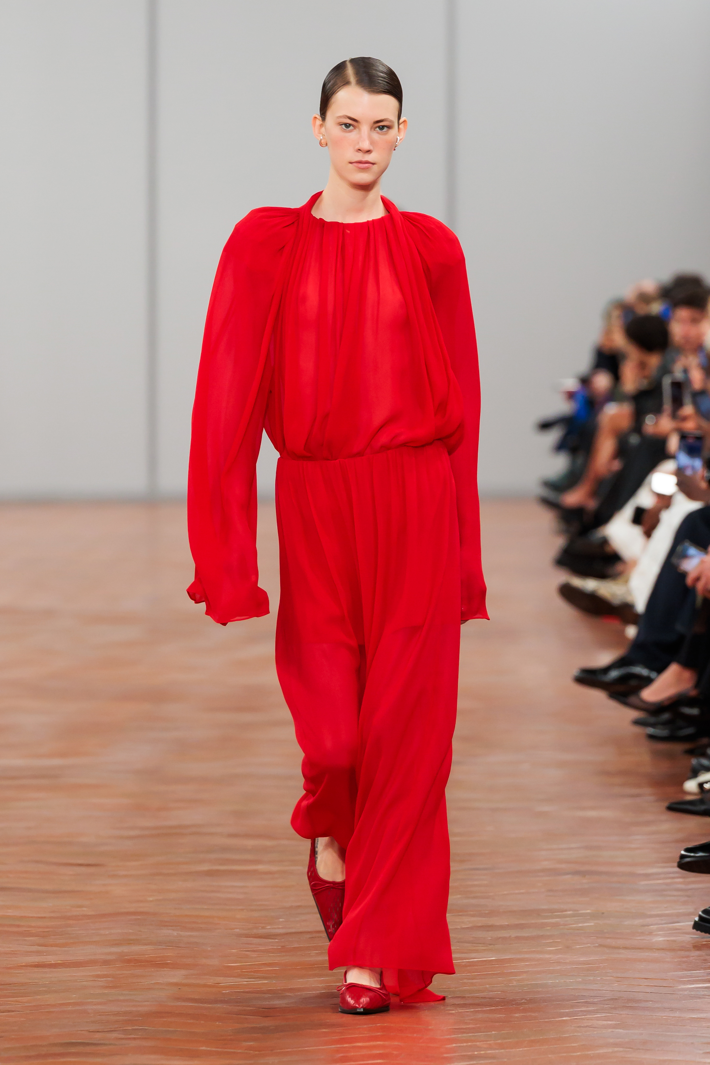 Model on runway in elegant red blouse and trousers with puff sleeves, standing confidently