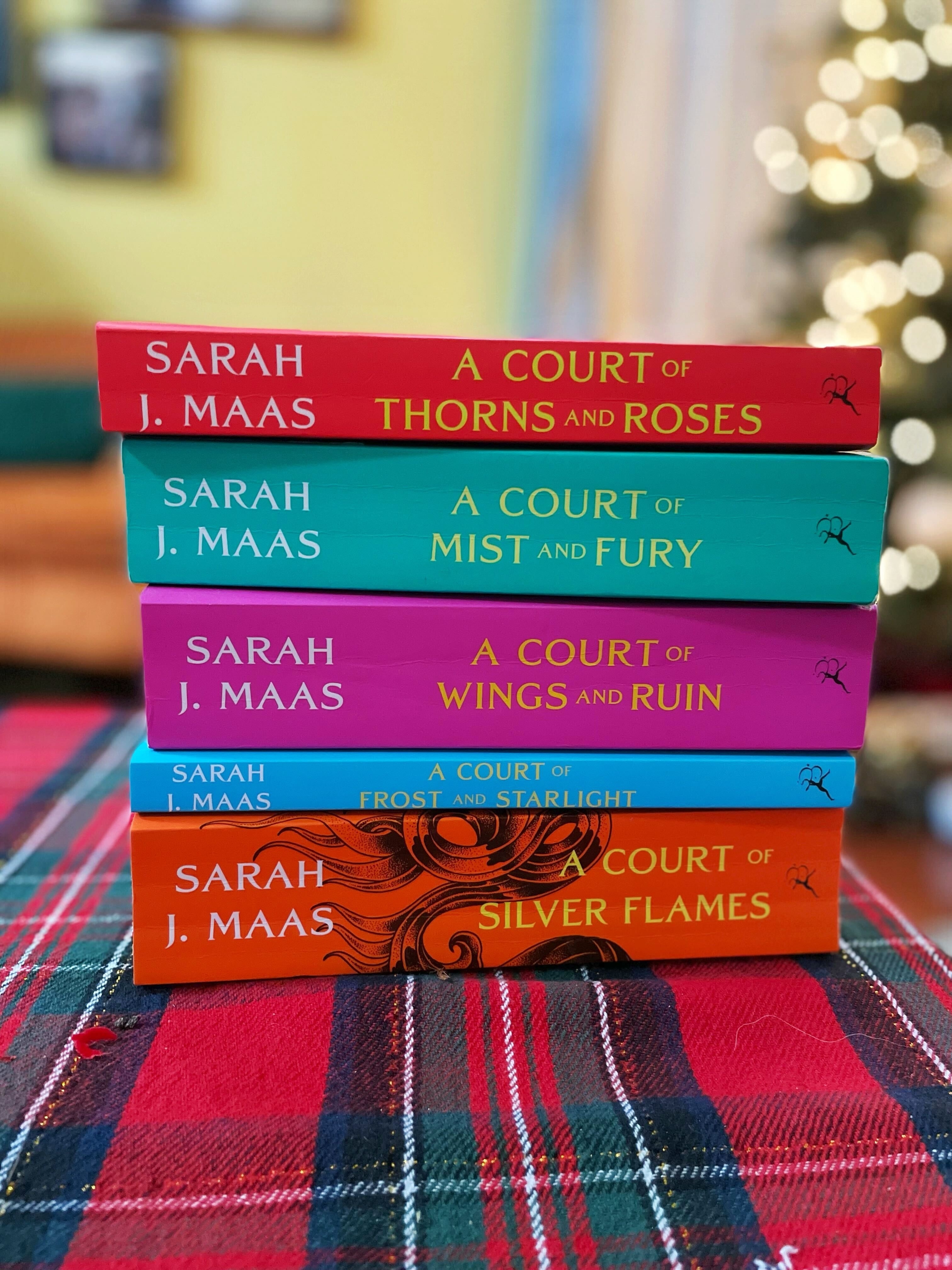 A stack of Sarah J. Maas books from "A Court of Thorns and Roses" series on a plaid surface