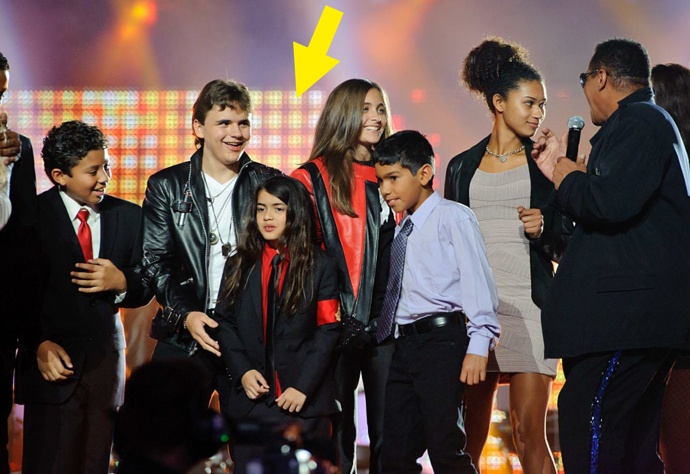 Group of smiling children on stage with a man holding a microphone speaking to them