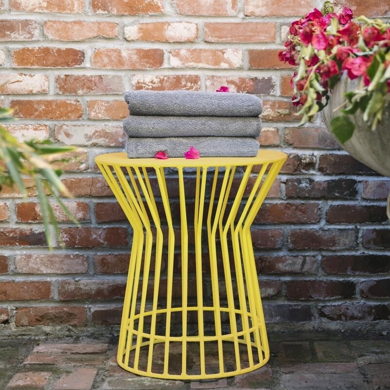 A yellow wire side table with a stack of folded grey towels on top