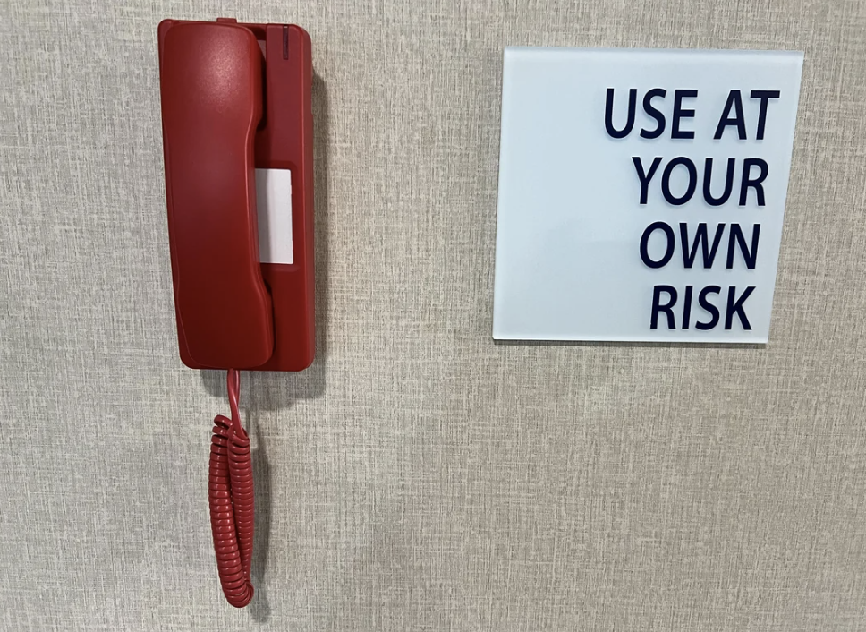 A red phone next to a sign that reads &quot;USE AT YOUR OWN RISK&quot;