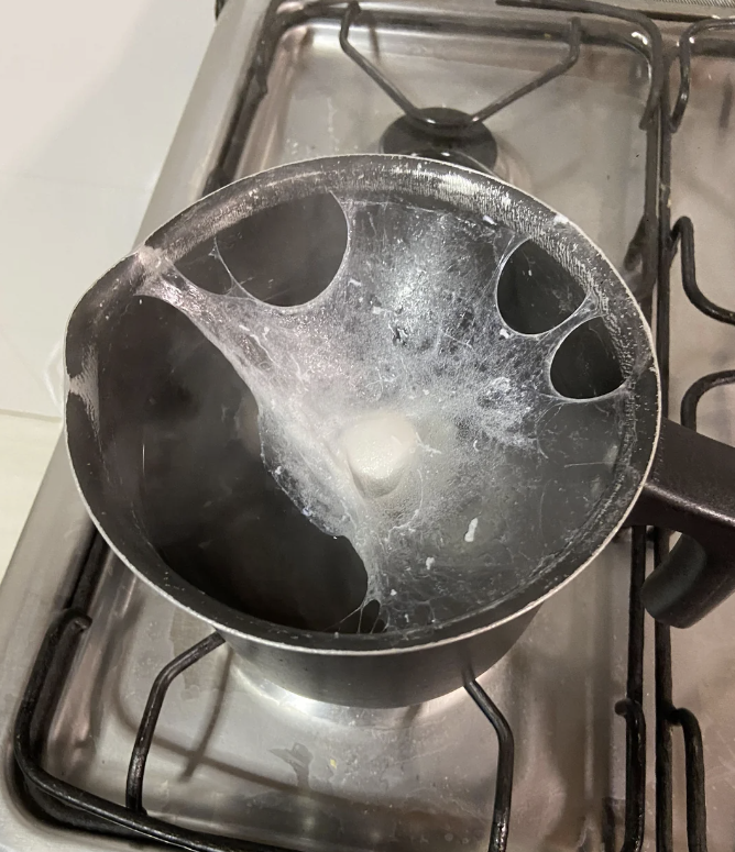 A used black saucepan with residues is placed on a stovetop burner