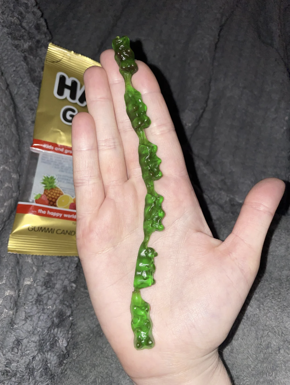 Hand holding a string of green gummy bears with an open candy bag in the background