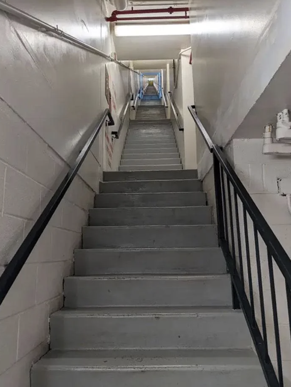 Staircase with handrails leading up to a bright exit door