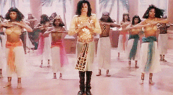 Michael Jackson in a gold and black outfit dancing with backup dancers in a music video setting