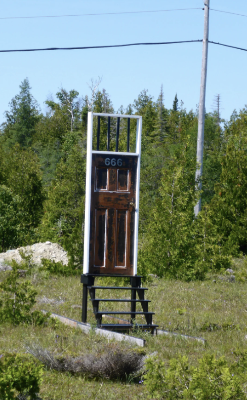 Door with the number 666 atop a staircase, surrounded by trees. No people in image