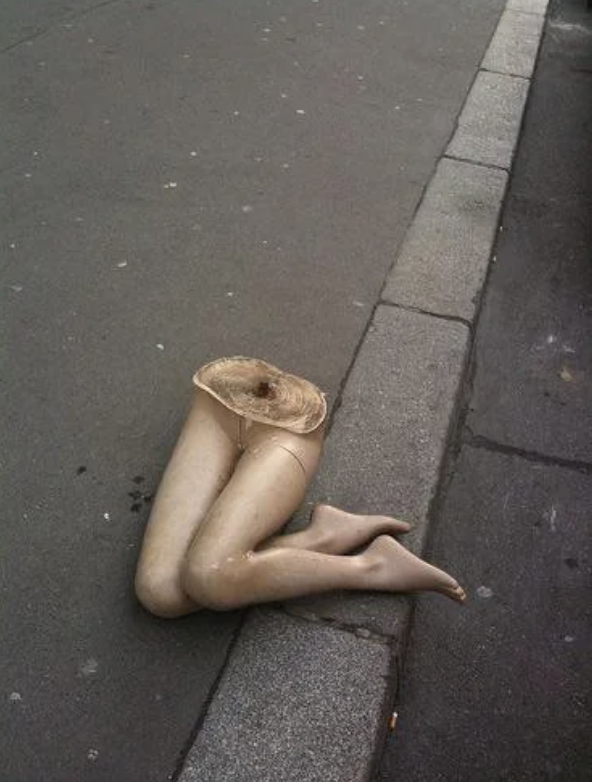 Mannequin legs discarded on a city sidewalk, positioned upright against the curb